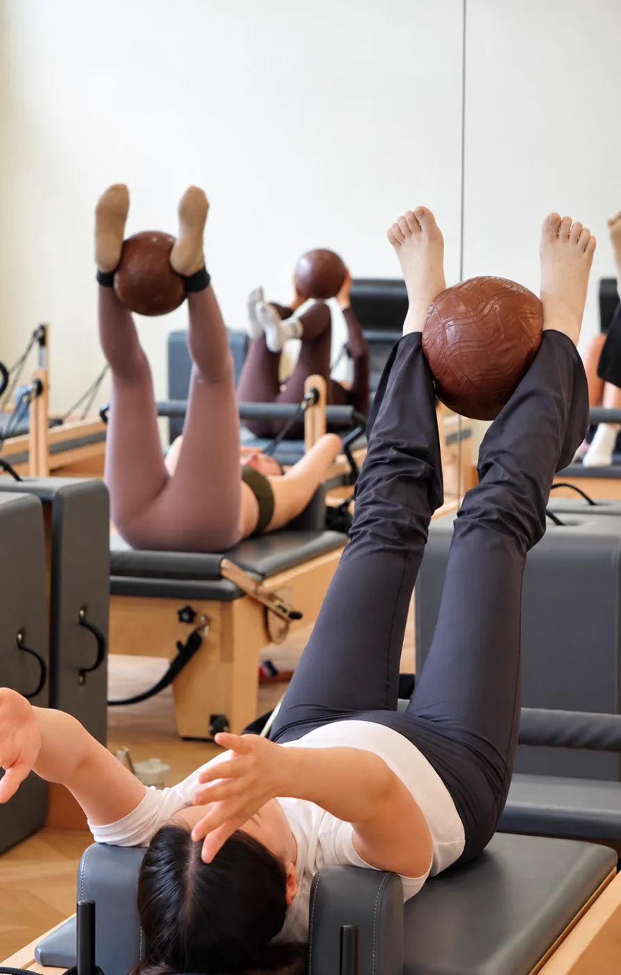 Cours collectif de Pilates Reformer, jambes levées avec un ballon